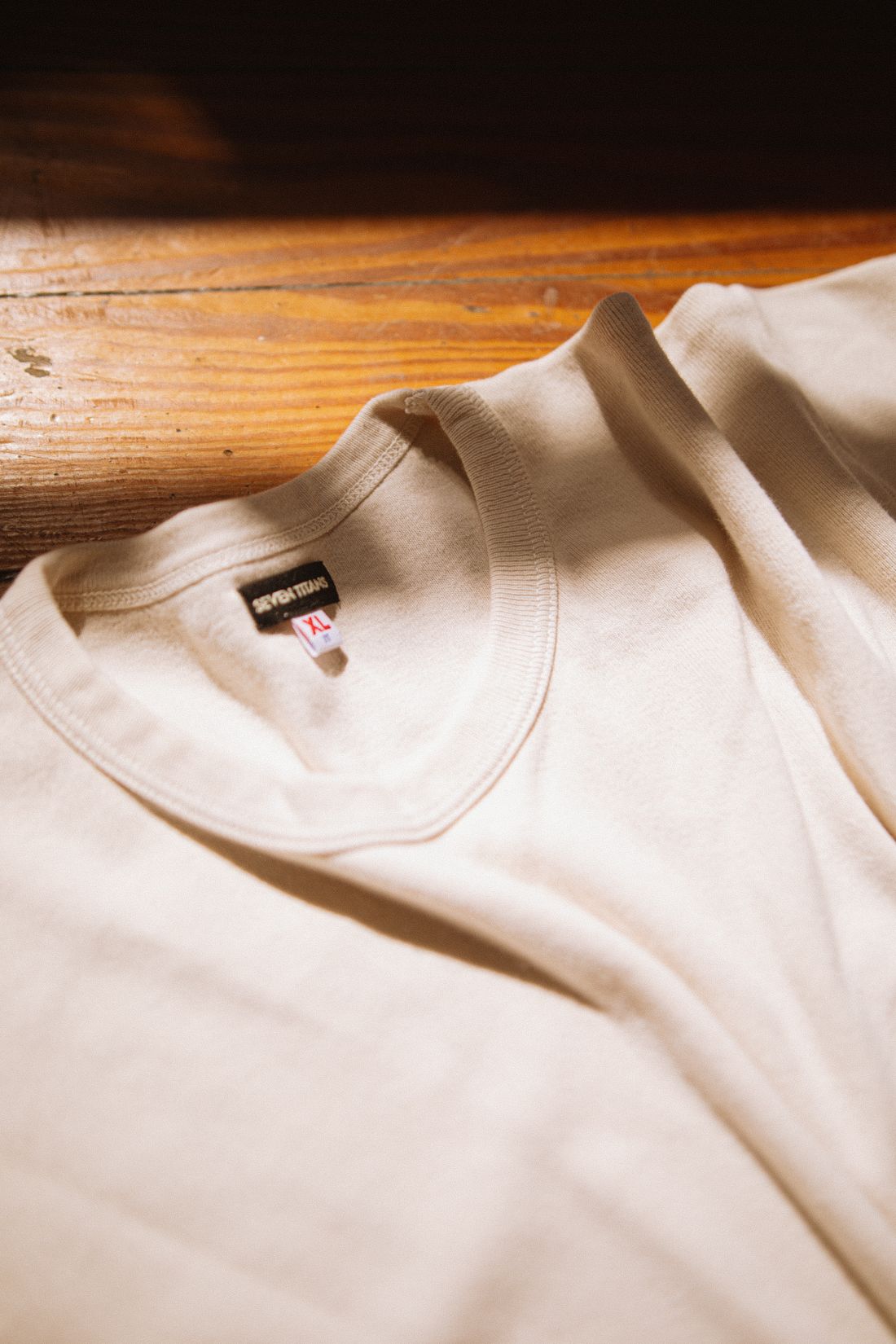 A cream heavyweight tee neckline resting on warm wood in soft light